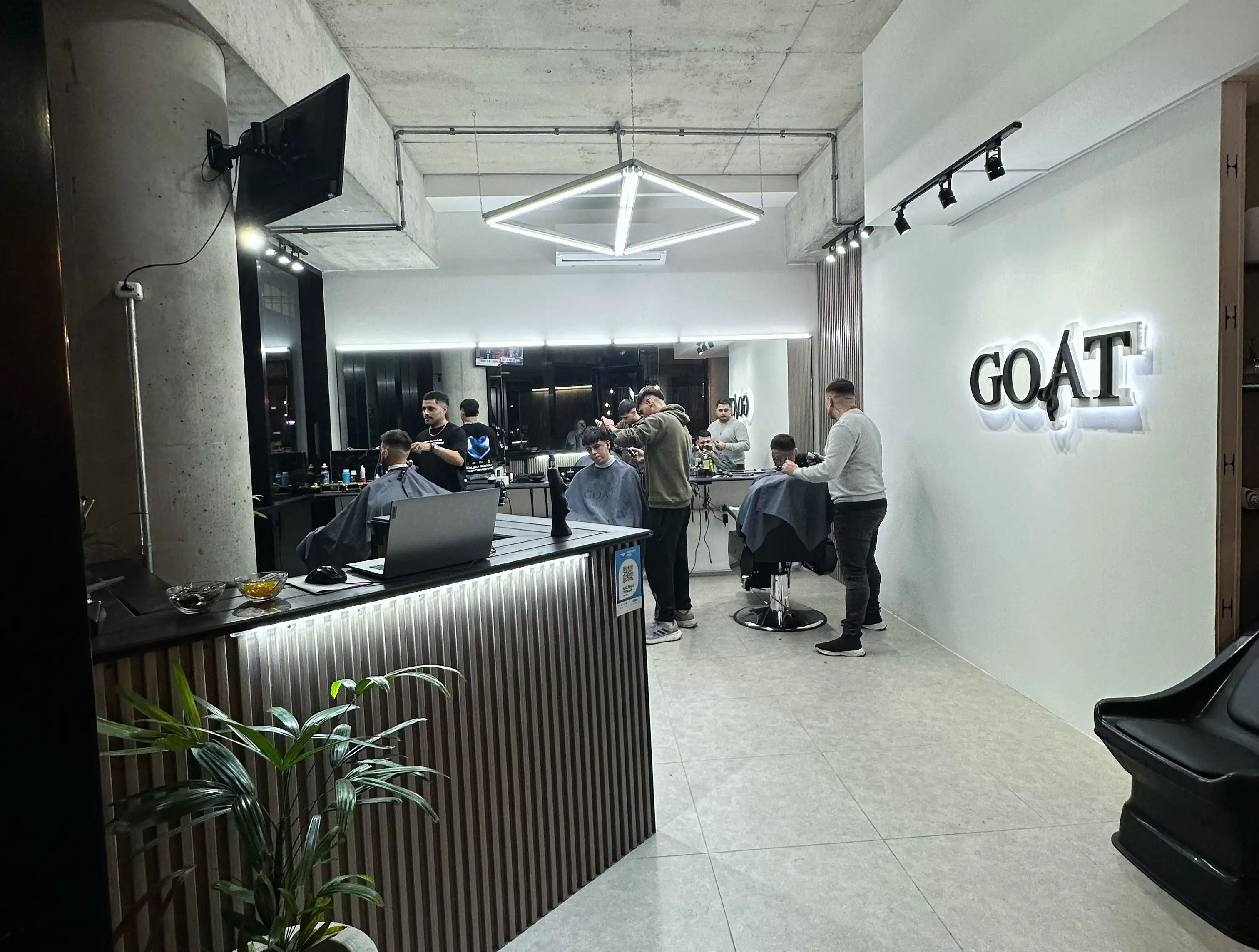 Tres estilistas trabajando en GOAT Barbería, cortando el cabello de tres clientes